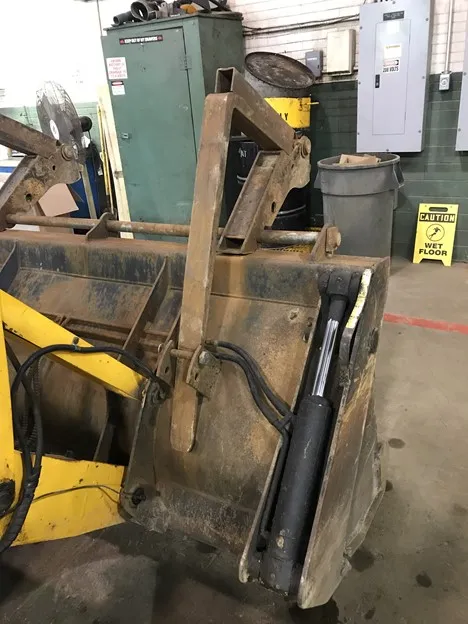 An image showing the rear view of a backhoe folding fork attached to a yellow PennDOT construction vehicle.